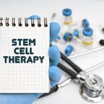 There is a stethoscope on the table, the doctor holds a notebook in his hand with the inscription – STEM CELL THERAPY