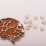 Alzheimer’s disease and mental health concept. Brain and wooden puzzle on a pink background